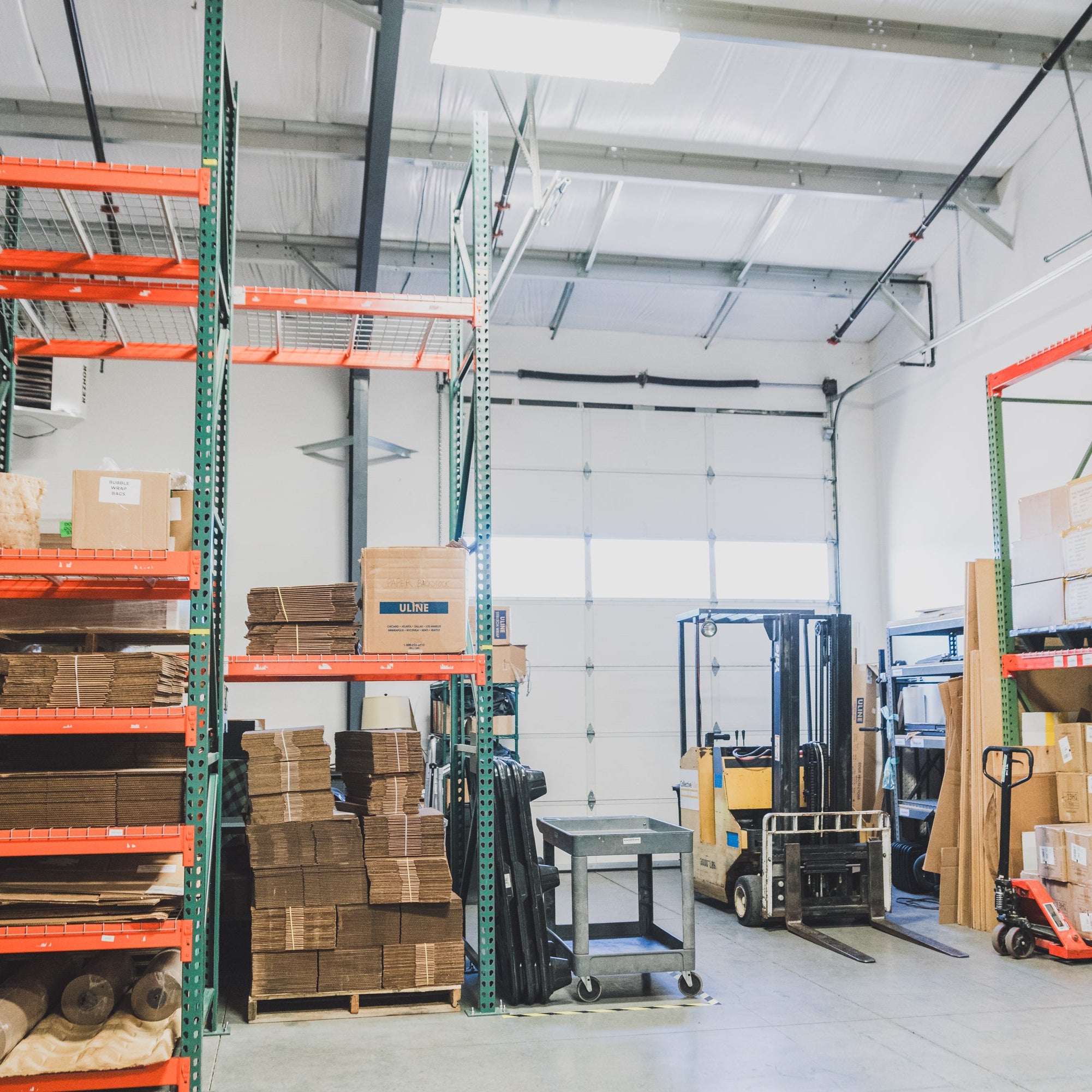 Collective Pallet warehouse space set up for cross docking operations with pallet racking, shipping materials, and warehouse equipment including a forklift and pallet jack.