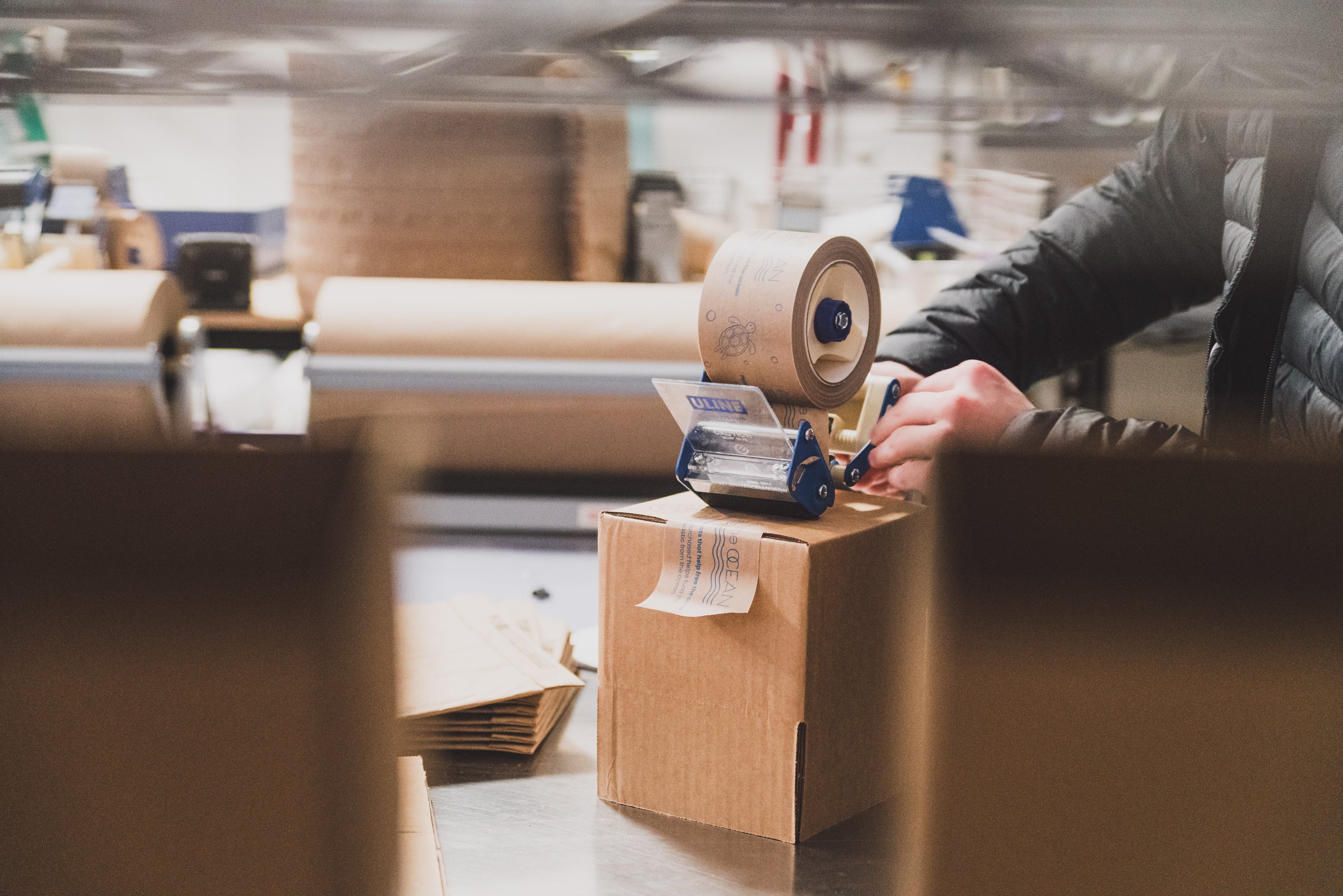 Close-up of a Collective Pallet team member sealing a shipping box at a warehouse packing station with recyclable packaging materials and fulfillment supplies.